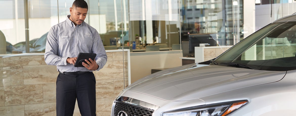 INFINITI Sales associate reviewing vehicle in dealership showroom. INFINITI Sales associate reviewing vehicle in dealership showroom.